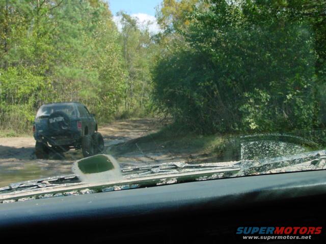 SUV stuck in mud on a dirt road, seen from inside another vehicle