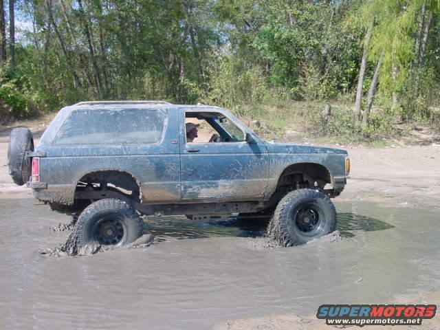 Mud-splattered blue SUV with a spare tire on the back, driving through a muddy puddle
