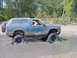 1992 Chevrolet S10 - A blue SUV navigates through a muddy terrain, with its tires deep in the water.
