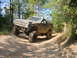 1992 Chevrolet S10 - A lifted, mud-covered Chevrolet Blazer K5 navigates a wooded trail with a person in the background.
