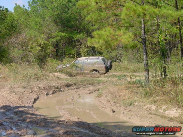 Off-road vehicle stuck in a muddy track surrounded by trees