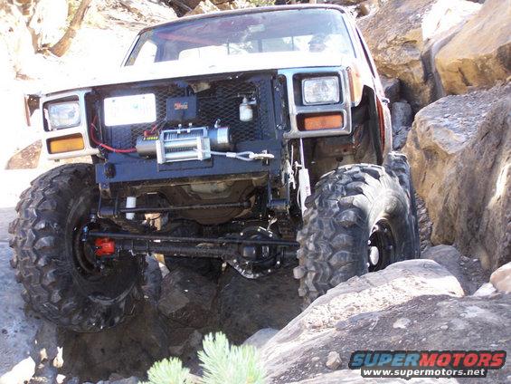 Off-road truck with large tires navigating rocks, has a winch mounted on the front