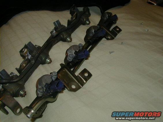 Two fuel injector rails with blue connectors on a textured surface