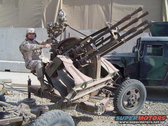 Soldier sits on a mounted Gatling gun with a military truck in the background
