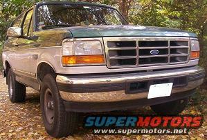 Green and silver Ford Bronco, front 3/4 view, parked outdoors on a dirt path with fallen leaves