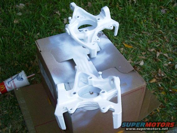 Two white painted suspension parts on a cardboard box with a McDonald's cup nearby