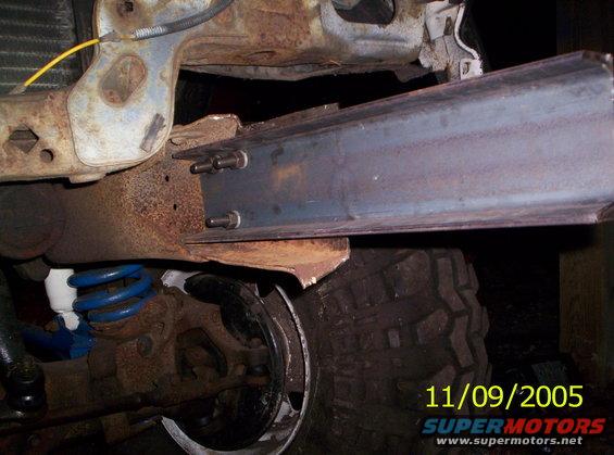 close-up of rusty vehicle frame with a metal beam bolted on, blue suspension spring visible
