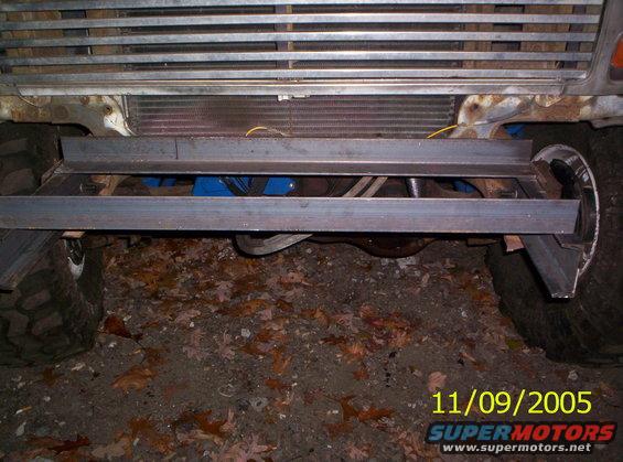 Front of a vehicle with a custom metal winch bumper being installed over the existing bumper area. Radiator and some suspension parts are visible