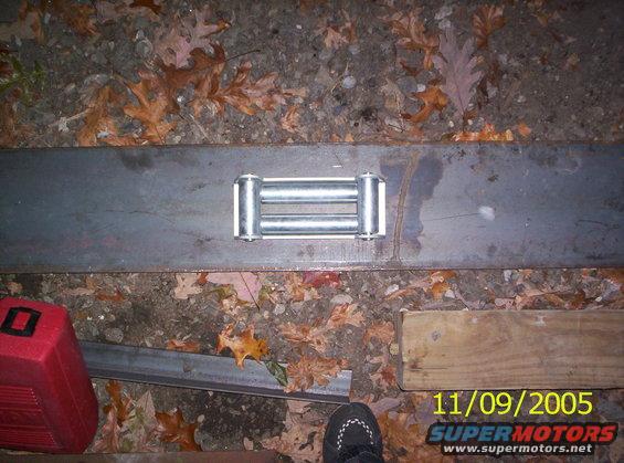 Winch roller fairlead on a metal plate, with leaves on the ground. A red toolbox is to the left