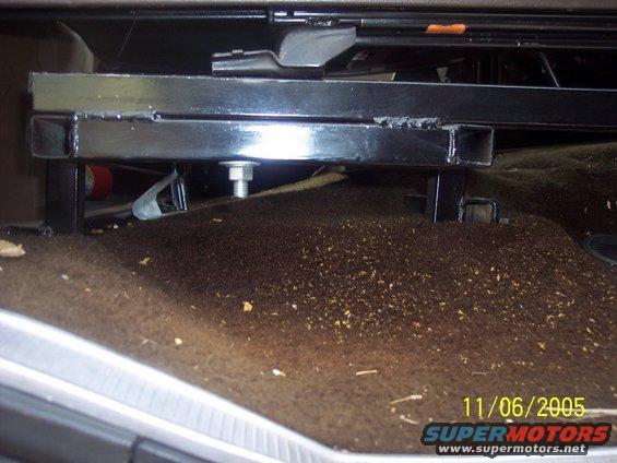 Black metal seat bracket with bolts on brown carpeted floor