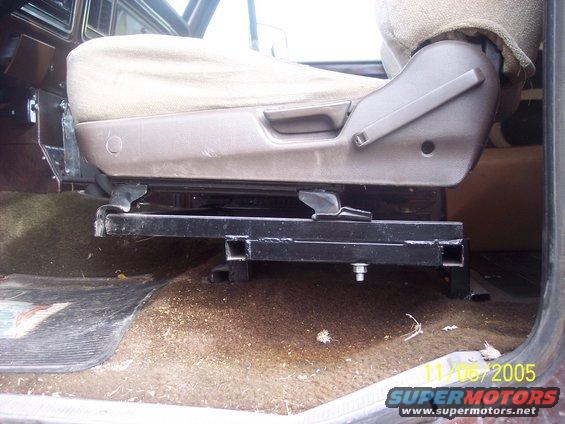 Custom metal seat bracket installed under a fabric seat in a vehicle interior