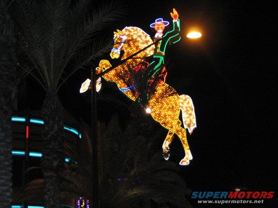 Neon cowboy riding a horse decoration at night with palm trees and building lights