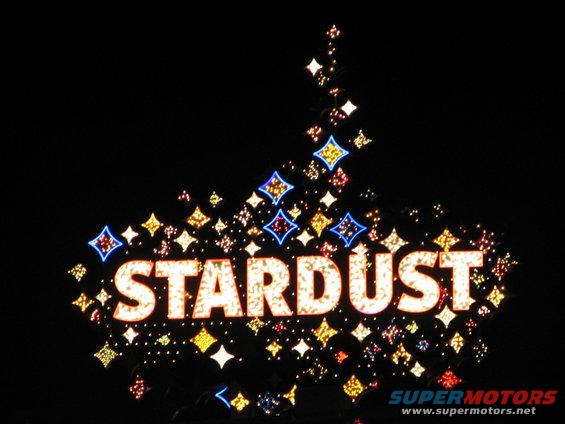 Stardust sign with illuminated letters and colorful starburst lights against a black night sky