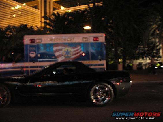 Black sports car driving past an ambulance at night