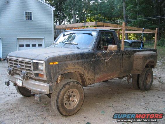 Black Ford F-350 dually pickup truck with a wooden rack over the bed, parked in a driveway