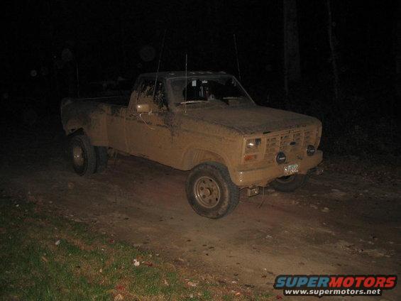 Mud-covered pickup truck with dual rear wheels parked on a dirt road at night
