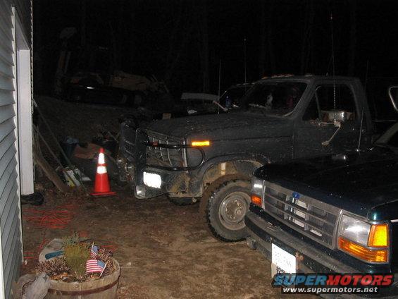 Dark colored 1980s Ford F-series pickup truck parked next to a newer model Ford pickup truck at night