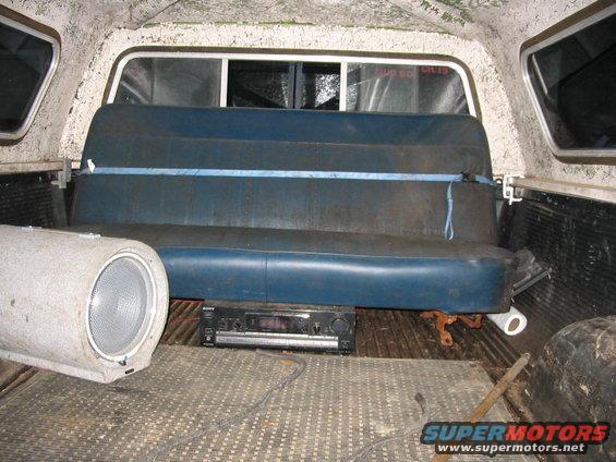 Pickup truck bed interior showing a blue bench seat, a large speaker, and a stereo receiver