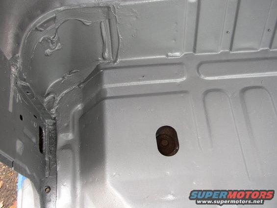 Gray painted vehicle floor with visible seam sealer and a bolt hole