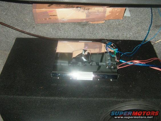 Car amplifier wired up on a subwoofer box in a trunk. Cardboard box behind it