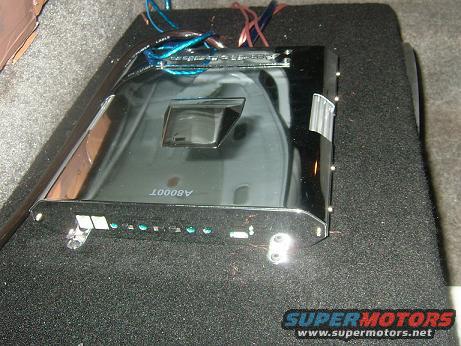 Car amplifier with chrome finish and blue wires, mounted on black carpet