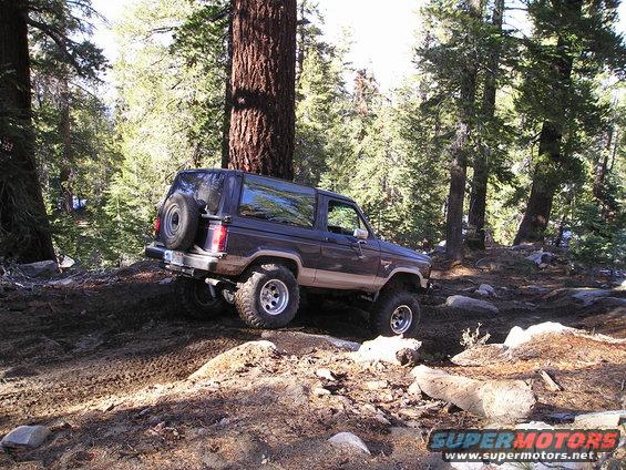 Dark blue and tan Ford Bronco II off-roading on a dirt trail with large tires and a spare tire on the back