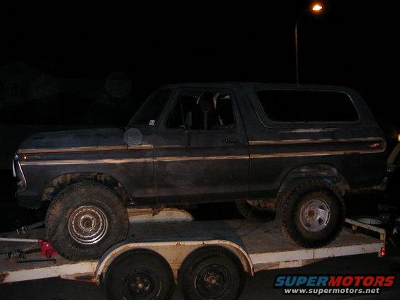 Dark blue 1978 Ford Bronco on a trailer, side view, with gold trim and off-road tires