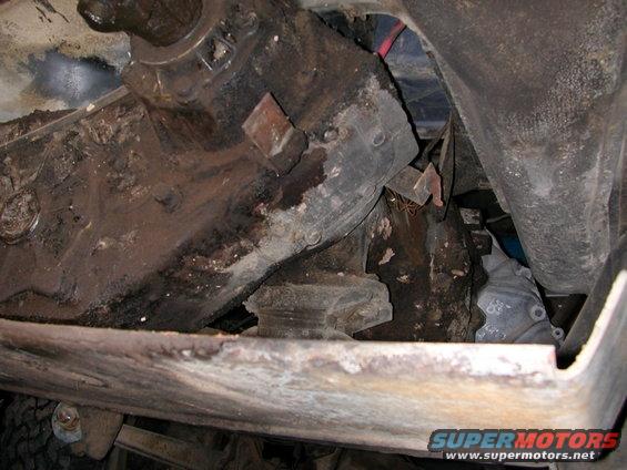 Underside of a vehicle showing rusty frame rails and some mechanical components
