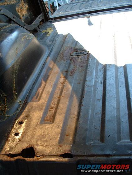 rusted out floor of a vehicle cargo area, showing metal panels and some holes from rust