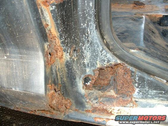 Rusted door frame with holes, showing black interior and gray exterior metal