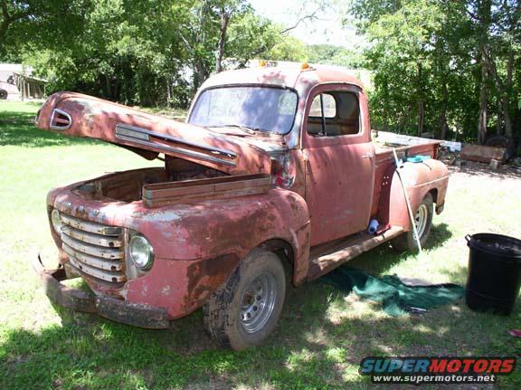 Rusty red pickup truck with hood open, front quarter view