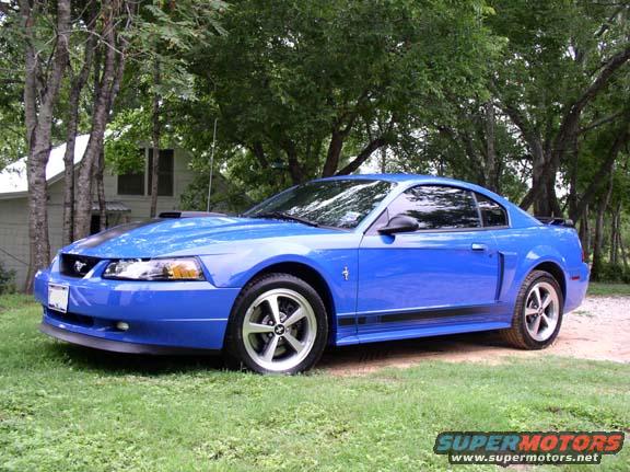 Blue 2000 Ford Mustang parked on grass near a house and trees