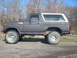 1986 Ford Bronco - This lifted Ford Bronco sits on a gravel road with trees in the background.
