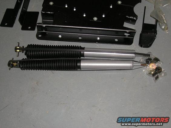 Two silver shock absorbers with black bellows and assorted metal mounting hardware in plastic bags