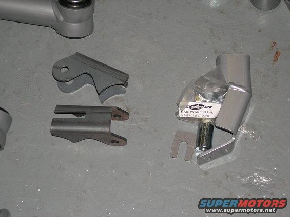 Metal brackets and a hardware kit for vehicle suspension, laid out on a gray floor