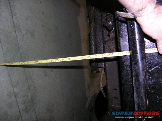 hand holding tape measure against vehicle frame, measuring length