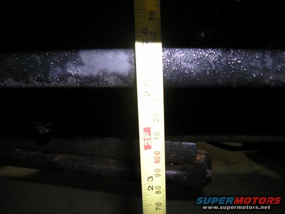 Yellow measuring tape against a dark vehicle frame, showing measurements in inches and centimeters