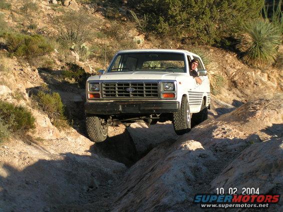 White Ford Bronco driving off-road, front view, tires on rocky terrain
