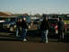 2002 Ford F-250 - A group of people gathered around several trucks and SUVs in a parking lot on a sunny day.