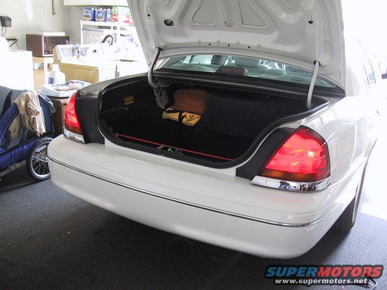 White Ford Crown Victoria's open trunk with items inside. Trailer and laundry area in background