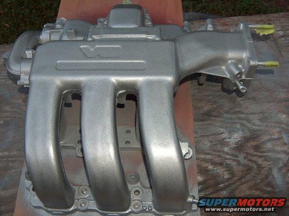Silver intake manifold with four runners, mounted on a wooden surface