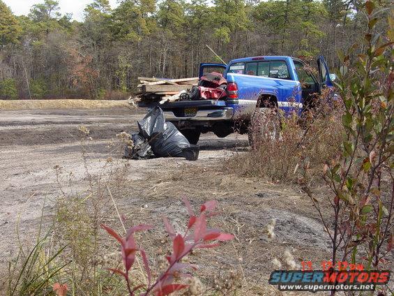 blue pickup truck with lumber and trash bags in the bed, parked in a dirt lot