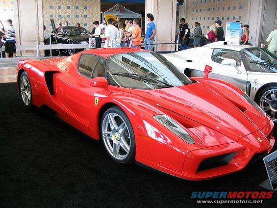 Red Ferrari sports car with a white car behind it. Signage visible