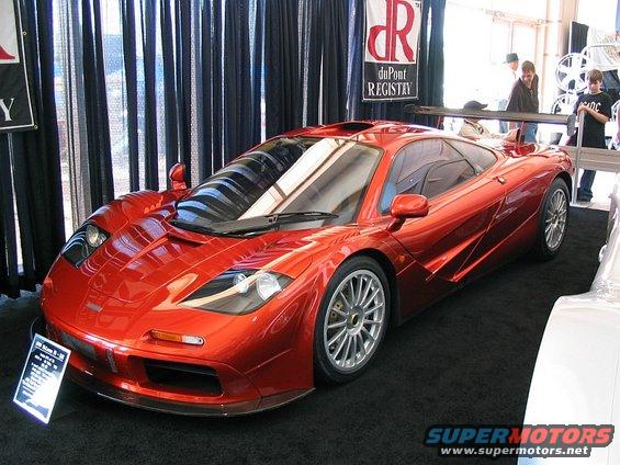 Red McLaren F1 sports car with a rear spoiler, viewed from the front three-quarter angle on a black carpet