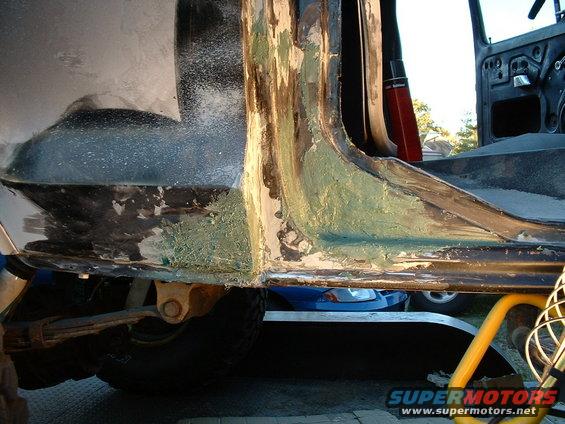 Close-up of rusted and repaired vehicle body panel, showing primer and body filler