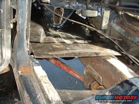 Interior floor pan with rust and a metal patch, showing brake and gas pedals