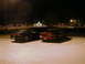 1994 Ford Probe - Two coupes are parked in a lot at night, with buildings and lights in the background.
