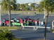 1994 Ford Probe - A group of people gather around a green 1994 Ford Probe with white racing stripes parked in a lot with other vehicles.