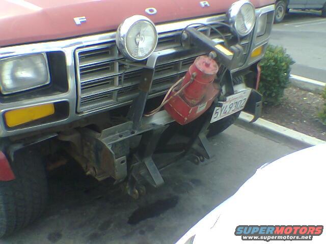 Red Ford truck front end with a winch and auxiliary lights, showing a chrome grille and yellow turn signals