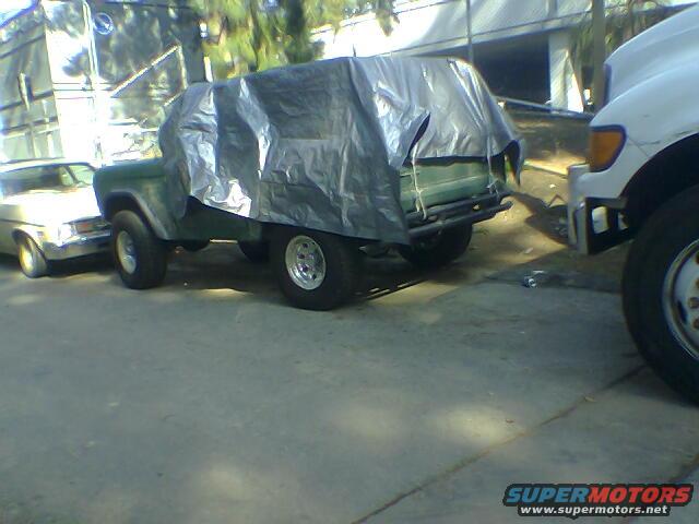 Green SUV covered by a tarp, parked next to a white truck and a light-colored car
